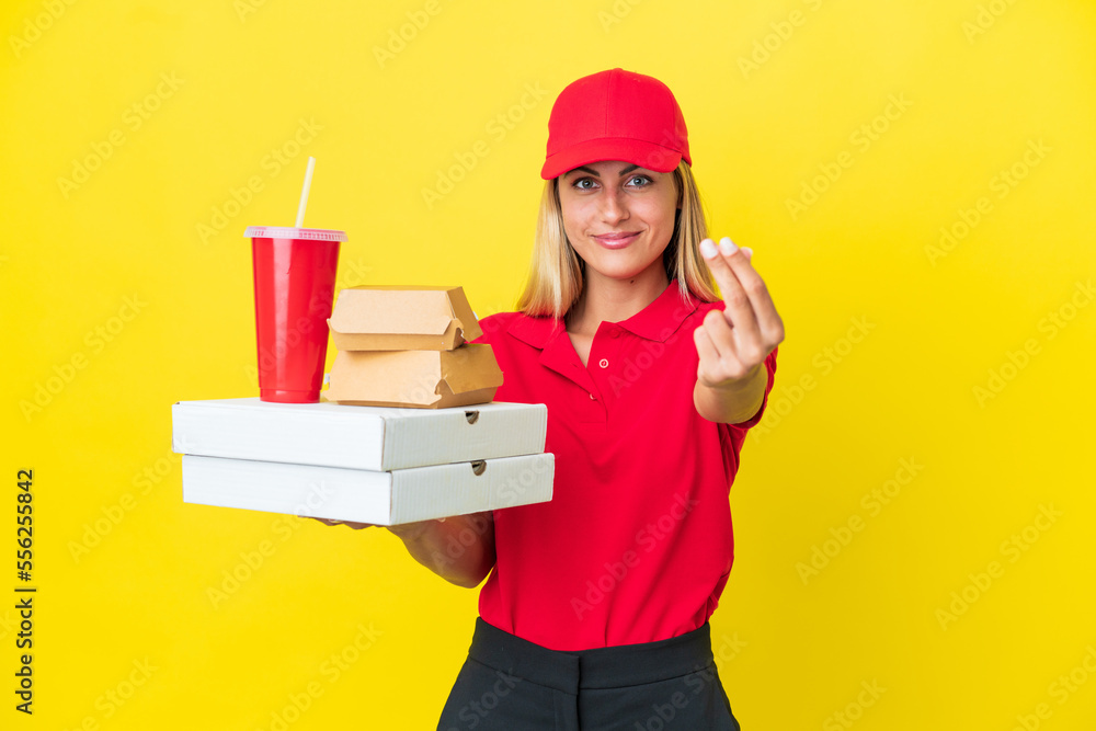 Delivery Uruguayan woman holding fast food isolated on yellow background making money gesture Delivery Uruguayan woman holding fast food isolated on yellow background making money gesture