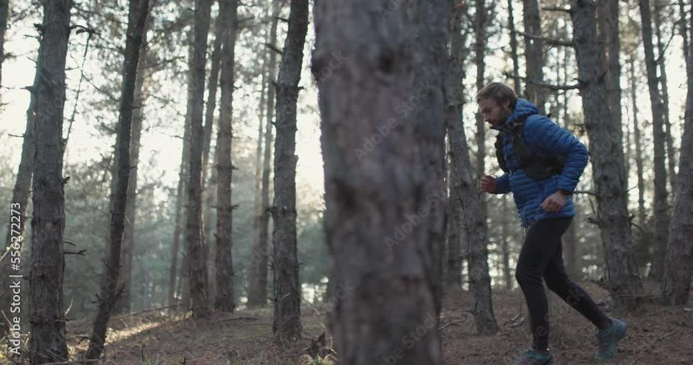 Trail runner in the woods wearing winter sports outfit. Man running on a forest path. Sun shining between trees. Recorded at 120 fps. Trail runner in the woods wearing winter sports outfit. Man running on a forest path. Sun shining between trees. Recorded at 120 fps.
