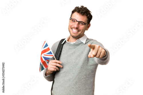Brazilian man holding an United Kingdom flag over isolated chroma key background pointing front with happy expression
