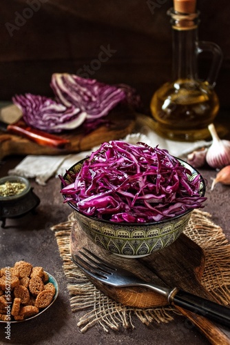 Red cabbage in a ceramic plate with a fork on a dark background. Red cabbage salad with oil and spices on a wooden board . The concept of vegetarian healthy food.