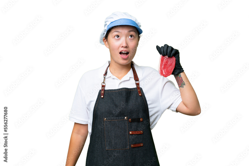 Young caucasian woman wearing an apron and serving fresh cut meat over isolated background looking up and with surprised expression Young caucasian woman wearing an apron and serving fresh cut meat over isolated background looking up and with surprised expression