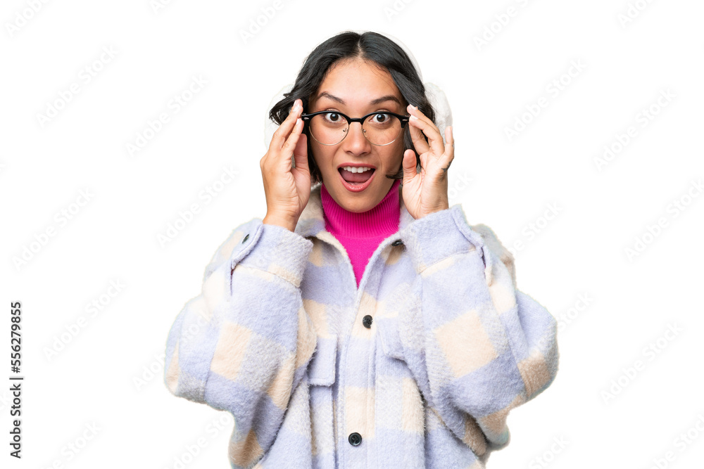 Young Argentinian woman wearing winter muffs over isolated background with glasses and surprised Young Argentinian woman wearing winter muffs over isolated background with glasses and surprised