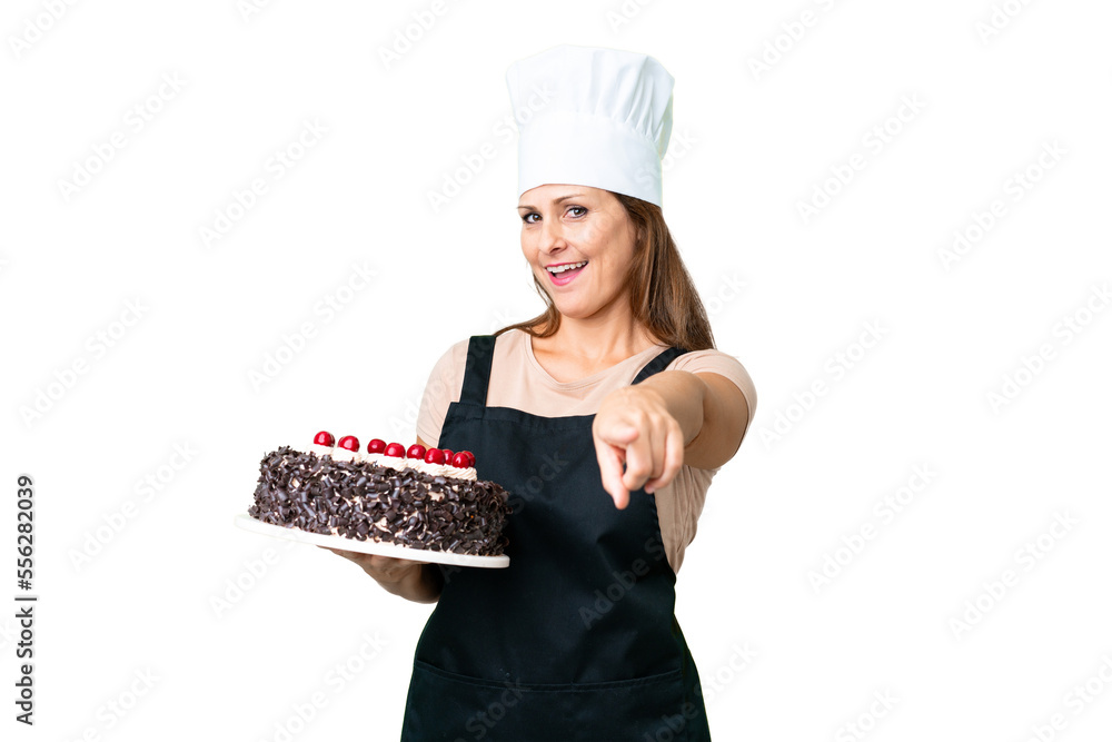 Middle age pastry chef woman holding a big cake over isolated background pointing front with happy expression Middle age pastry chef woman holding a big cake over isolated background pointing front with happy expression