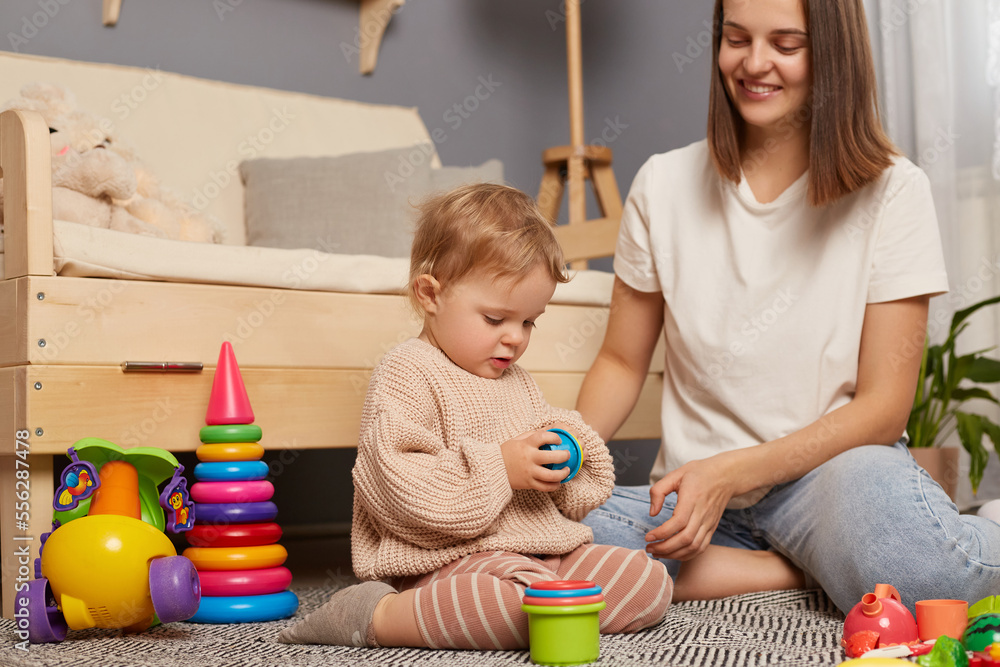 Young mother and little baby assembling plastic toys, method early development, confident family constructing toy tower use self educational game at home. - obrazy, fototapety, plakaty 