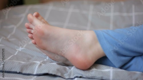 Bare feet of a girl on a blanket. The girl in pajamas lies on the bed.