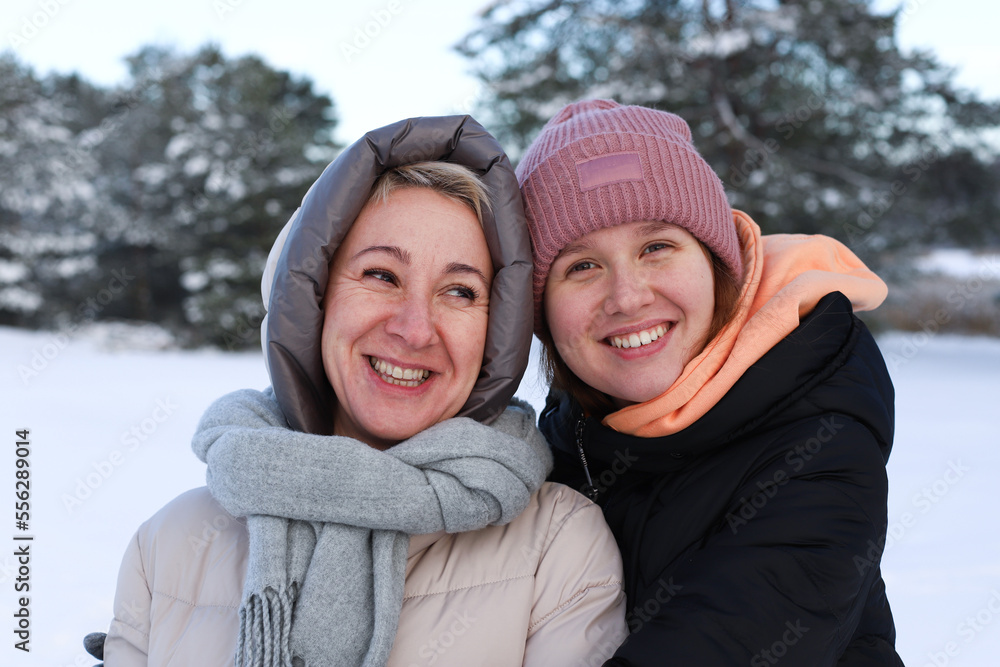 Concept of happy family, old age, emotions, walk in the winter forest of mom and adult daughter hugging outside. Woman smile. Around the green pine forest background of Christmas tree in forest.