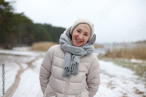 Portrait of happy beautiful elderly senior retired woman in age is playing, having fun with snow outdoors in forest or park at winter cold day, smiling, enjoy weather