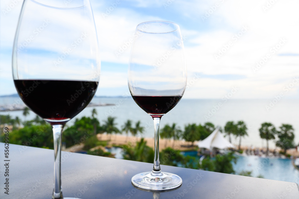 A glass of red wine on black table against the backdrop of the summer beach. Glasses of red wine on vacation. Wine tasting and relaxation at the resort. Copy space.