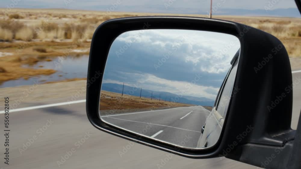 Car is driving along road passing through valley surrounded by mountains. Rearview mirror shows highway behind auto, ridge, power lines. Automobile moving across steppe with yellow grass in autumn Car is driving along road passing through valley surrounded by mountains. Rearview mirror shows highway behind auto, ridge, power lines. Automobile moving across steppe with yellow grass in autumn