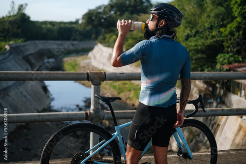 A young bearded cyclist drinking from a drinking bottle.