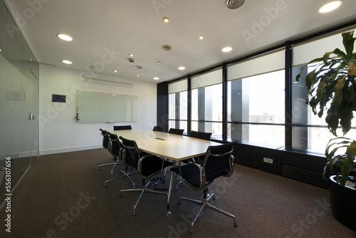 Boardroom with long wooden table with black swivel chairs and wall with windows