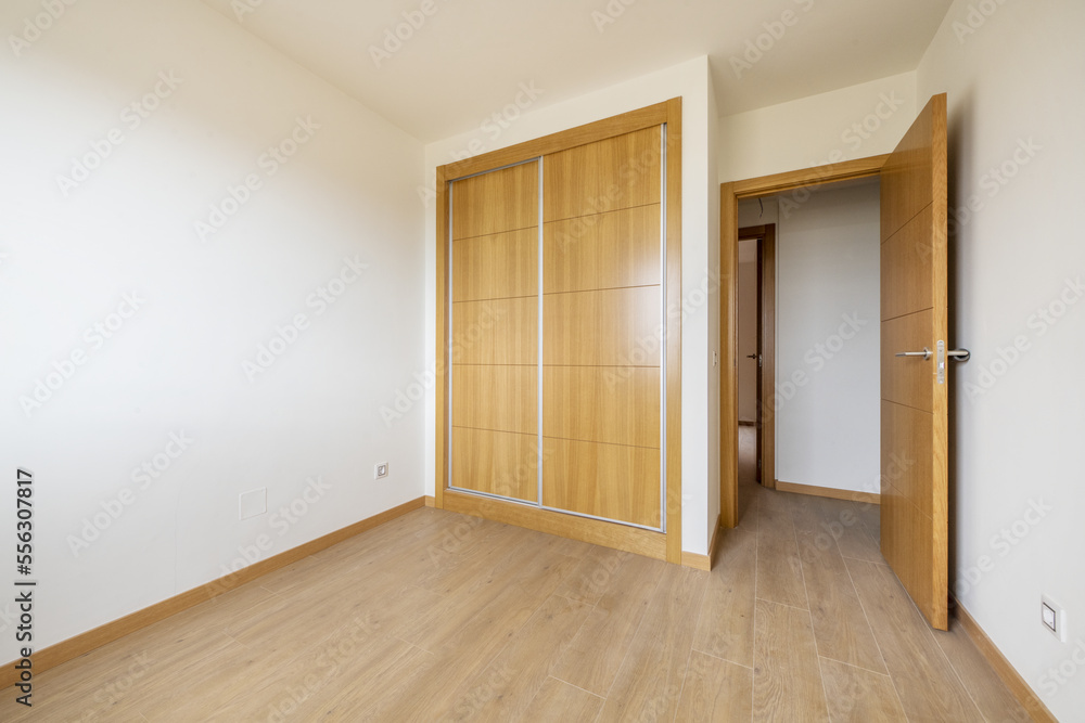 Obraz premium bedroom with two-section built-in wardrobe with large oak sliding doors and wooden floor and access door of the same material