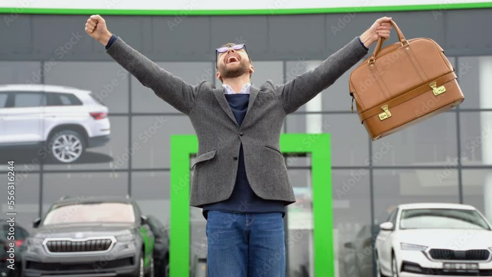 A man shows emotions of happiness after buying a new car near a car dealership A man shows emotions of happiness after buying a new car near a car dealership