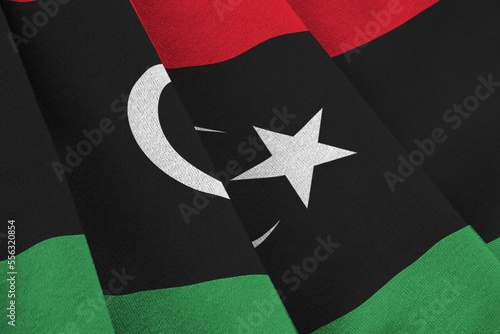 Libya flag with big folds waving close up under the studio light indoors. The official symbols and colors in fabric banner