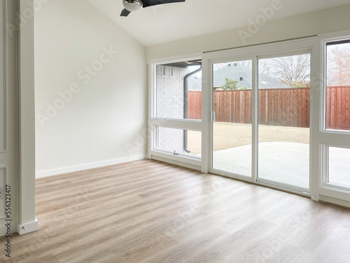 Empty white sunroom with wall of windows to backyard, vaulted ceilings, light wood floors, light and bright empty space