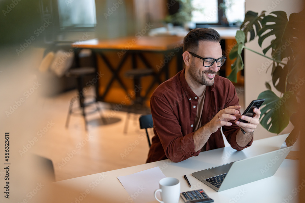 Shot of a young businessman using a smart phone in a home office. Smiling, touching the screen, browsing the internet. Shot of a young businessman using a smart phone in a home office. Smiling, touching the screen, browsing the internet.