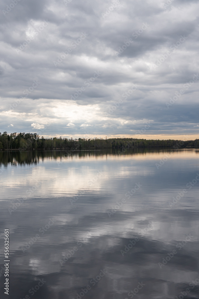 A beautiful lake in spring, dynamic grey sky, clouds. Reflection in the water. Place for rest.