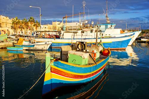 Traditional fishing boats luzzu in Marsaxlokk village in Malta, painted in bright colours – blue, red and yellow. Warm, afternoon sunlight