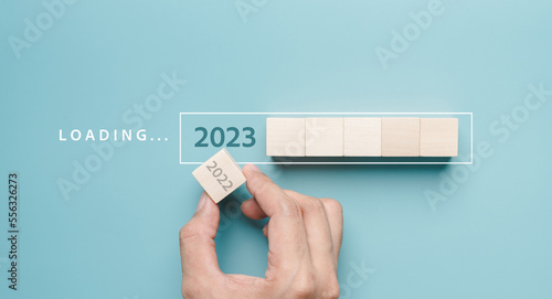 Hand putting wooden cube block for loading progress from 2022 to 2023 to countdown merry christmas and happy new year concept...