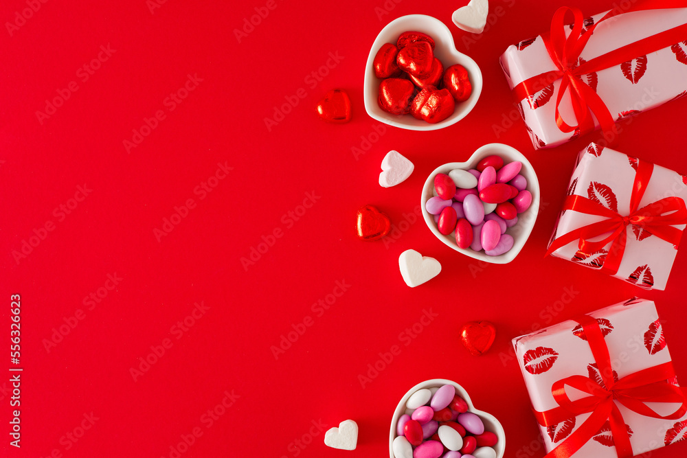 Love Valentines concept. Top view composition made of gift boxes and heart shaped saucers with confectionery chocolate candies and lollipops on red background. Flat lay with copy space.