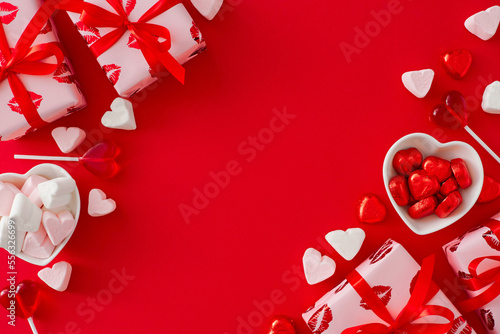 Love Valentines concept. Flat lay photo of gift boxes, heart shaped saucers with sweets candies and lollipops and marshmallow on red background with copy space. Valentines card idea.