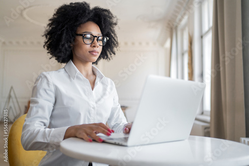 A young woman with glasses and a white shirt in the office is typing a message using a laptop. A freelancer is working on a new online project site.