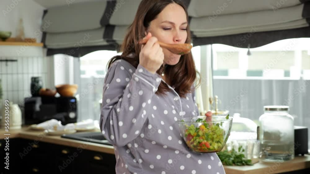 Pregnant woman stirs and eats healthy salad with chopped vegetables. Brown-haired housewife enjoys taking care about health and baby in belly, close-up Pregnant woman stirs and eats healthy salad with chopped vegetables. Brown-haired housewife enjoys taking care about health and baby in belly, close-up