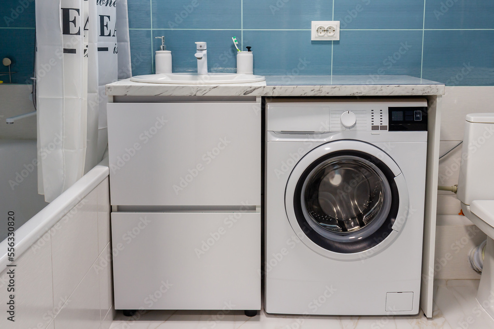 Spacious bathroom with large bathtub, white vanity unit with drawers for washbasin and washing machine. Spacious bathroom with large bathtub, white vanity unit with drawers for washbasin and washing machine.