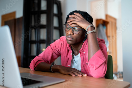 Fotografía Oppressed depressed African American man closed eyes sits at table with laptop stressed due to lack interest in work