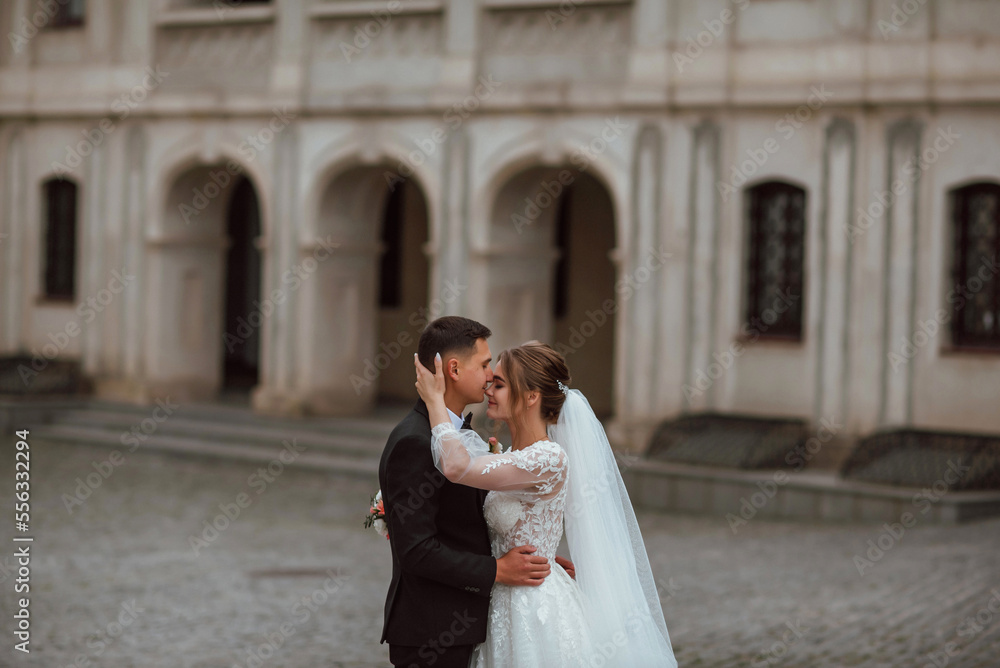 newlyweds in love on their wedding day pose for a photographer against the background of nature; he is in a dark classic jacket and she is in a white dress; a very happy and cheerful couple of people 