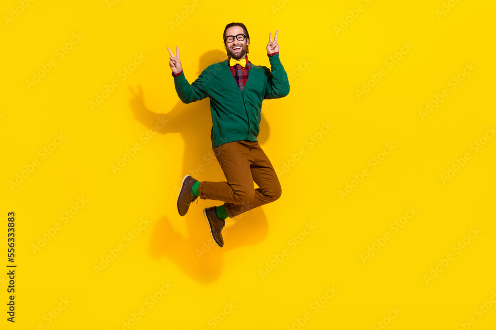 Full length photo of excited crazy man jumping demonstrate v-sign isolated on yellow color background