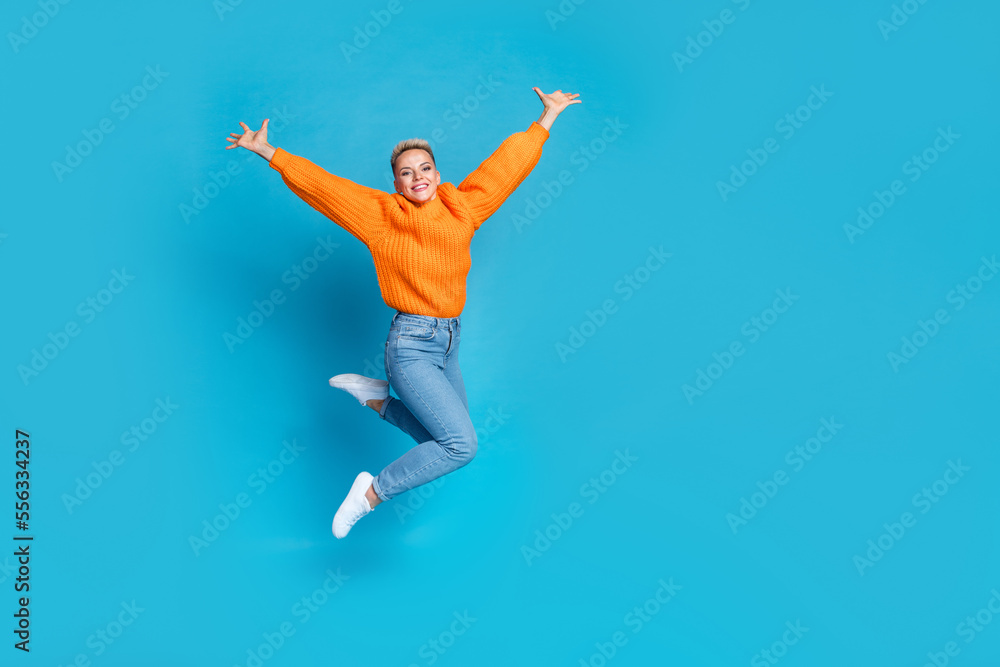 Full length photo of sweet cheerful lady wear orange sweatshirt jumping high rising arms empty space isolated blue color background