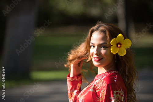 Beautiful young woman in a typical Moroccan red suit, embroidered with gold and silver threads, with a yellow pacific flower in her hair. Concept beauty, ethnicity, typical suits, Marrakech, Arab.