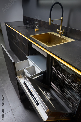 Dishwasher and kitchen waste bin cabinet. Pull out kitchen drawers for waste bin separate waste collection and Dishwasher under golden sink basin and facet black glass electric hob stoneware toptable. photo