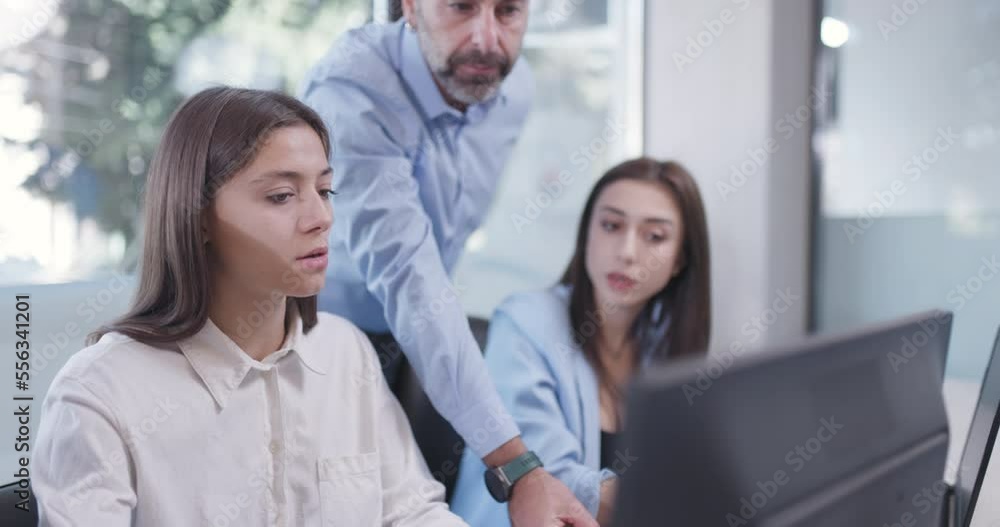 Young bussiness colleagues working in an office. Senior supervisor standing and giving advice. Successful team solving a problem. Young bussiness colleagues working in an office. Senior supervisor standing and giving advice. Successful team solving a problem.
