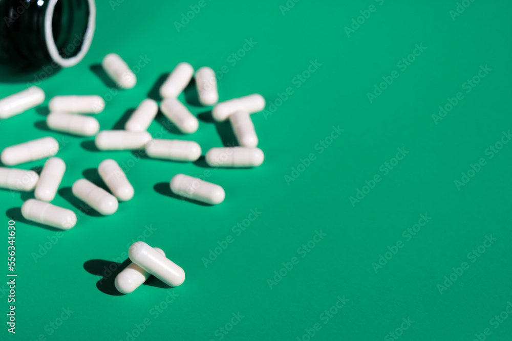 close up of white pills capsules and bottle on green background close up of white pills capsules and bottle on green background