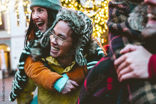 happy multiracial friends walking at city street on winter holiday-Young people having fun together outdoors wearing warm clothes-Cheerful smiling couple on piggyback move-Lifestyle Friendship concept
