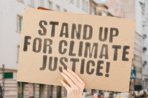 The phrase " Stand Up for Climate Justice! " is on a banner in men's hands with blurred background. Protection. Recycling. Sign. Smoke. Stay. Support. Sustainability. Sustainable. Urgency. Warming