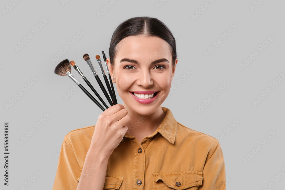Happy woman with different makeup brushes on light grey background Happy woman with different makeup brushes on light grey background