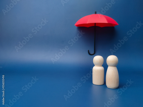 A couple of wooden dolls are hiding under a red umbrella  protecting wooden peg dolls  planning  saving families  preventing risks and crises  health care and insurance concepts.