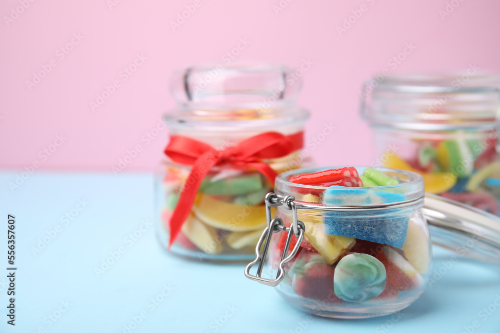 Tasty colorful jelly candies in glass jars on light blue table against pink background. Space for text Tasty colorful jelly candies in glass jars on light blue table against pink background. Space for text