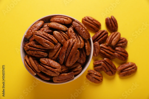 Tasty pecan nuts with bowl on yellow background, flat lay