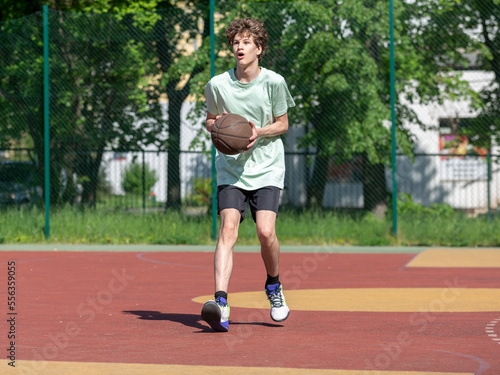 Teenager running in the stadium. Cute young teenager in t shirt with a ball plays basketball on court. Sports, hobby, active lifestyle for boys  © Natali