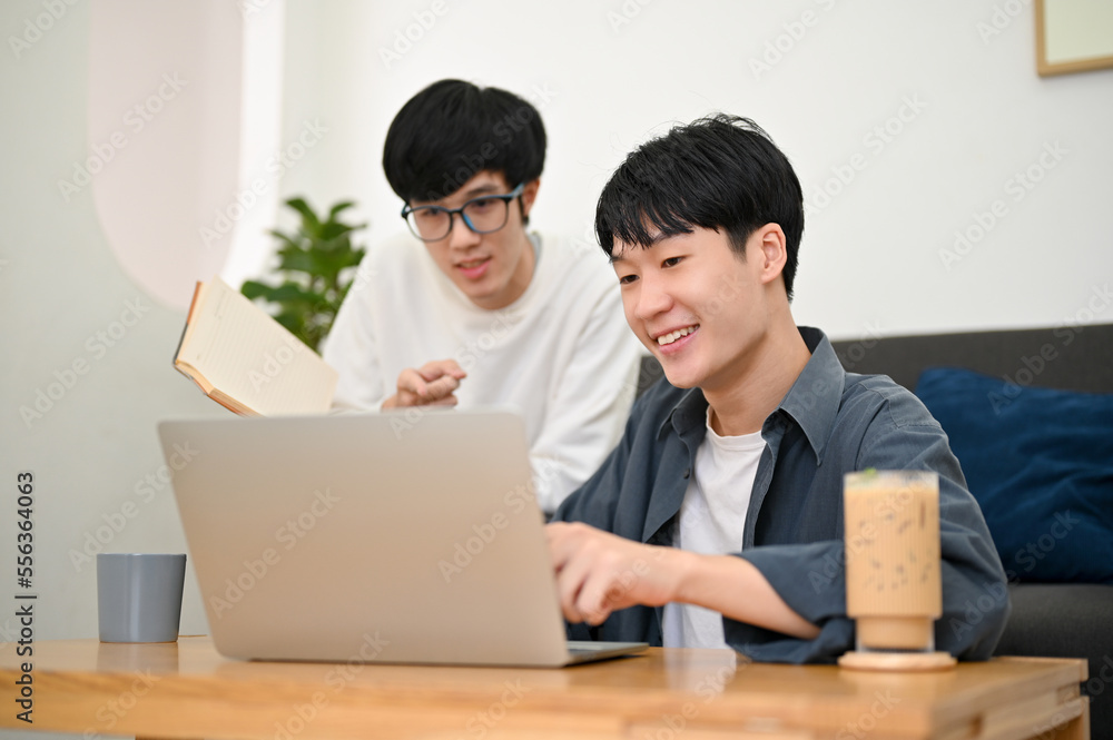 Two Asian male students looking at laptop screen, doing a project together, planning their presentation Two Asian male students looking at laptop screen, doing a project together, planning their presentation