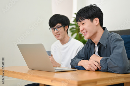 Two of smart young Asian male college students looking at laptop screen. side view