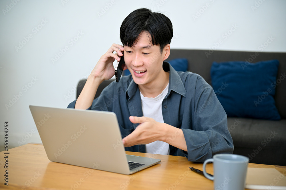 Happy handsome Asian male freelancer talking on the phone with his client. work from home Happy handsome Asian male freelancer talking on the phone with his client. work from home