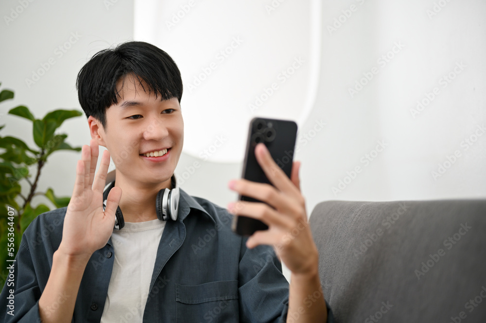 Happy Asian man enjoys talking on video call with his friend while relaxing in the living room. Happy Asian man enjoys talking on video call with his friend while relaxing in the living room.