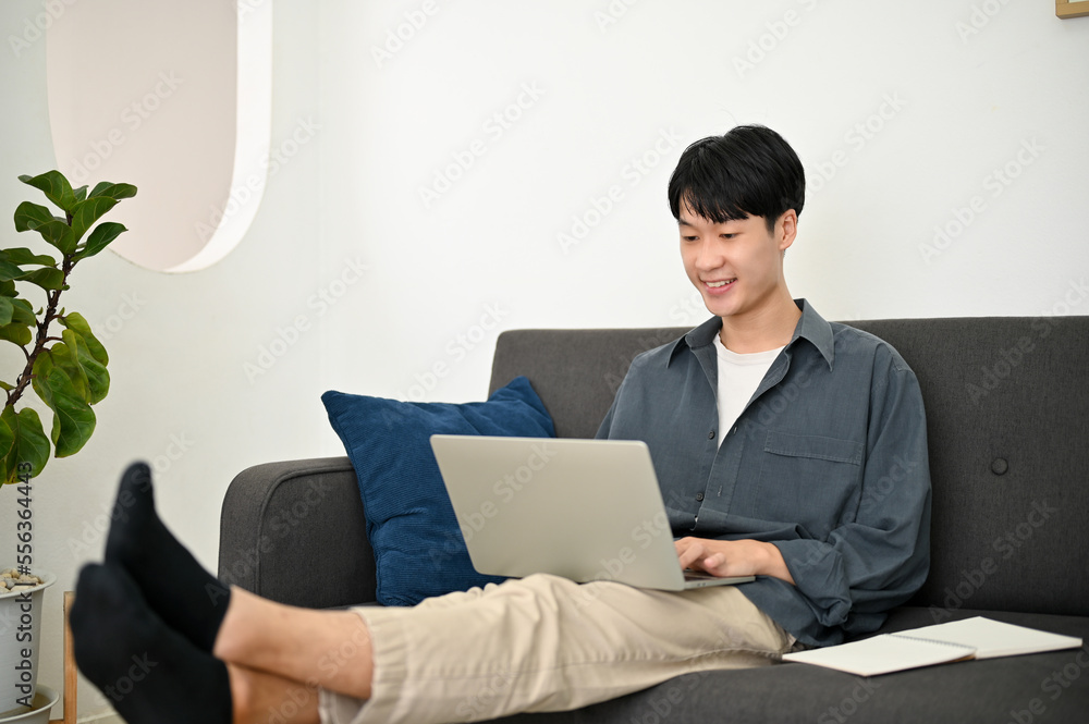 Relaxed and chilling young Asian man remote working from home, using laptop on sofa Relaxed and chilling young Asian man remote working from home, using laptop on sofa