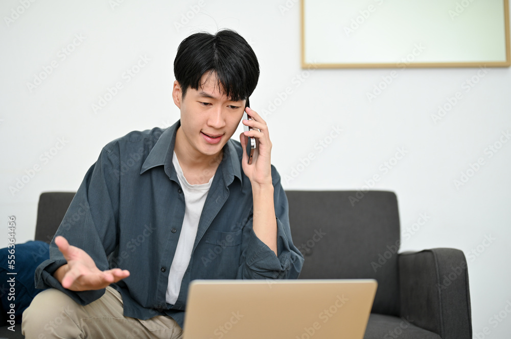 Stressed Asian male looking at laptop screen while having a serious conversation over the phone. Stressed Asian male looking at laptop screen while having a serious conversation over the phone.