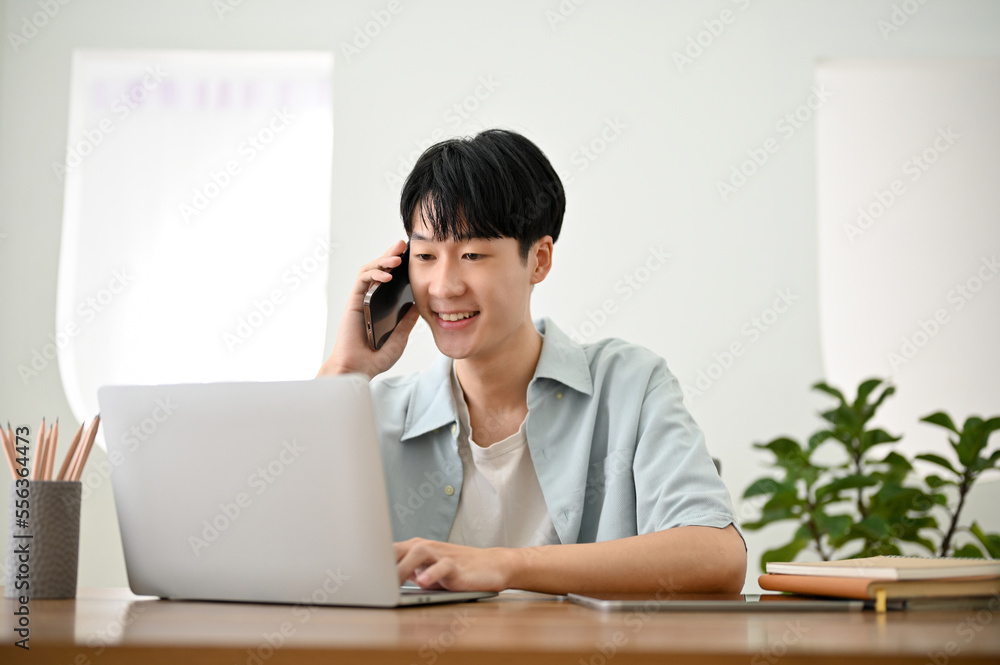 Handsome Asian man talking on the phone and using his laptop computer. work from home Handsome Asian man talking on the phone and using his laptop computer. work from home